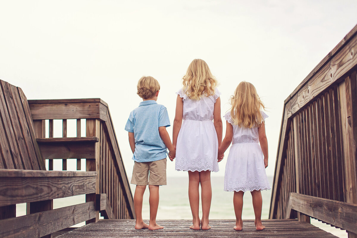 siblings holding hands on boardwalk overlooking beach