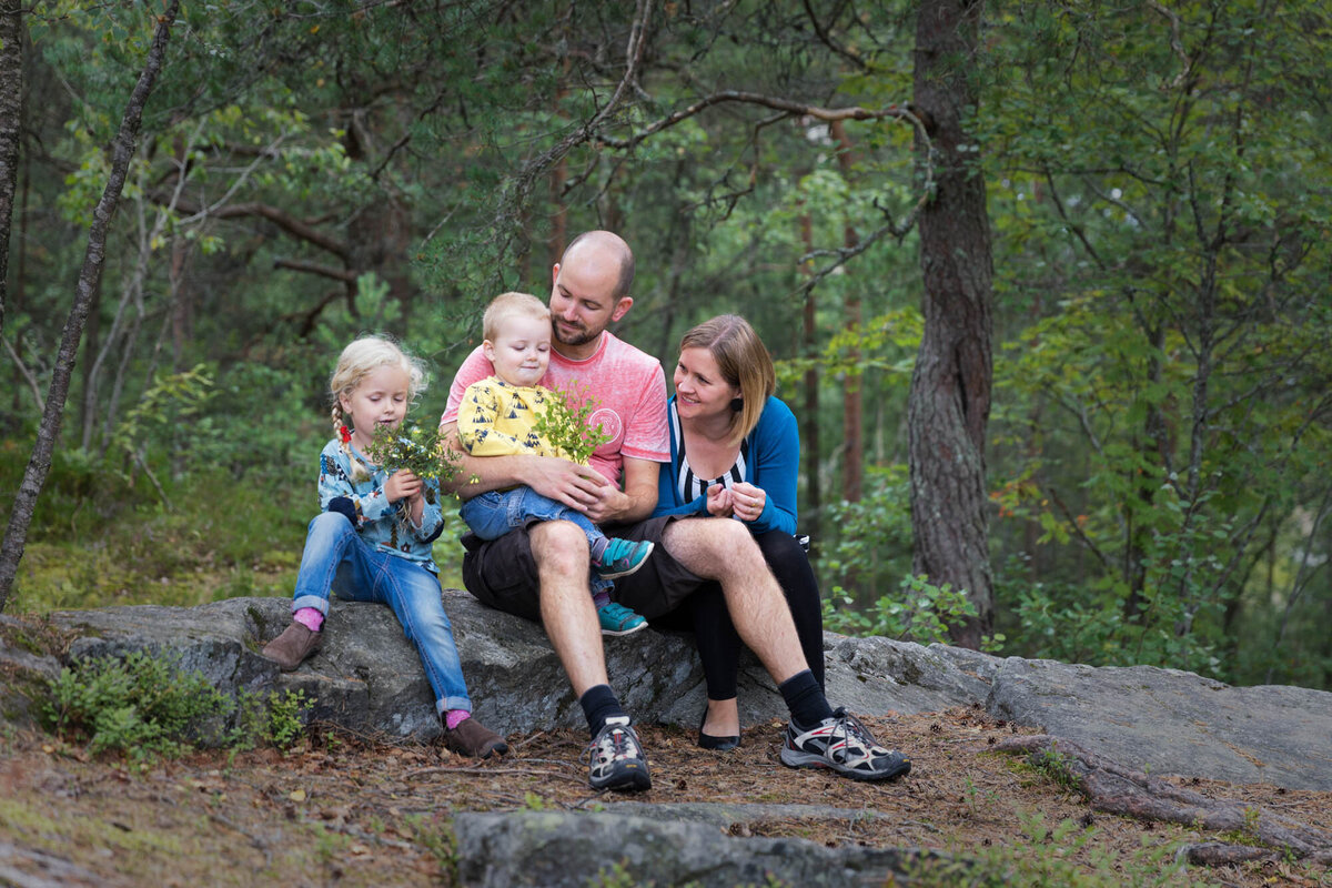 Livsstilsfoto familieportrett av familie som sitter på et berg i en skog.