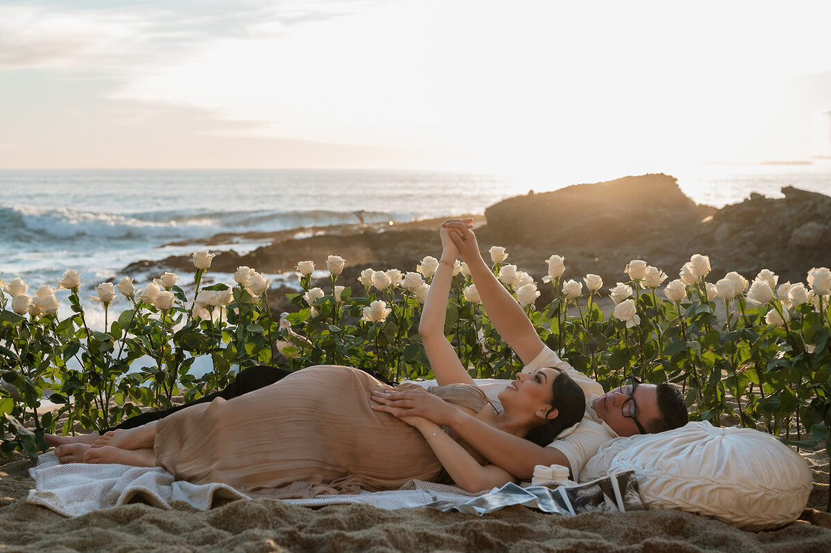 photo of mom and dad laying in a bed of flowers oceanside during family photos
