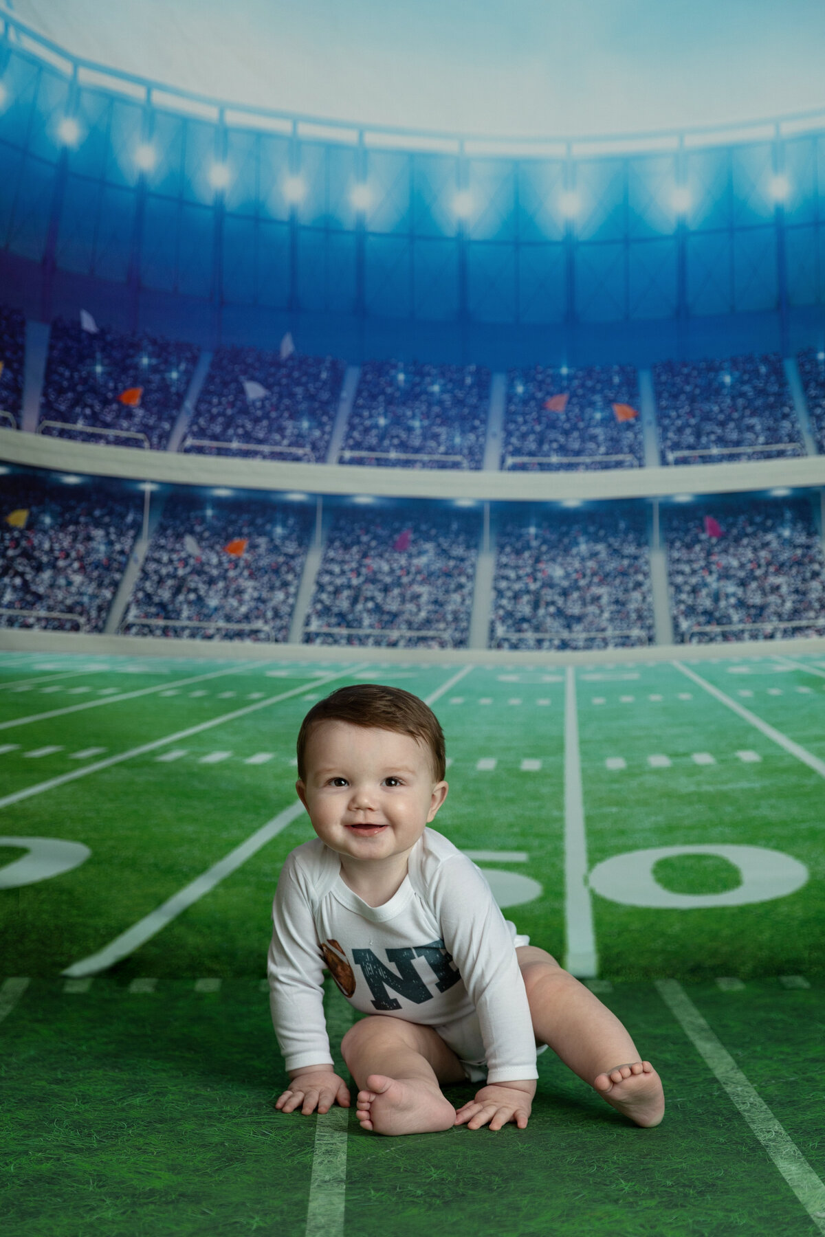 A toddler boy crawls on a football field in a studio