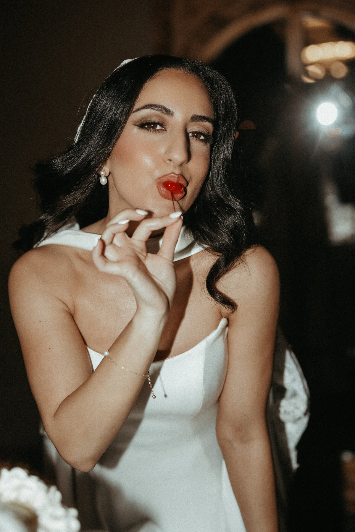 Bride in a modern satin wedding dress playfully poses with a cherry at Le Venere wedding venue, captured by Minnesota wedding photographer Clewell Photography in a glamorous editorial style