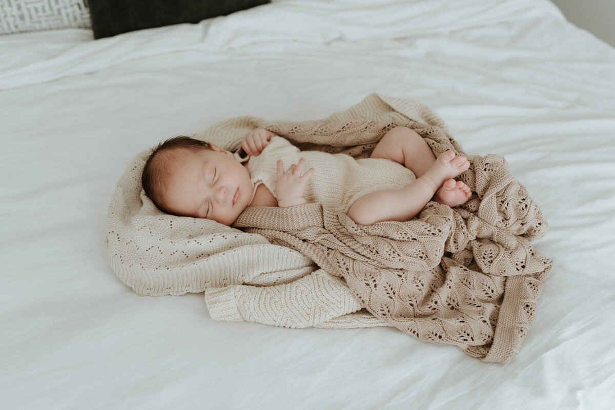 A newborn sleeps soundly in a nest of blankets on a bed in a Brisbane home.