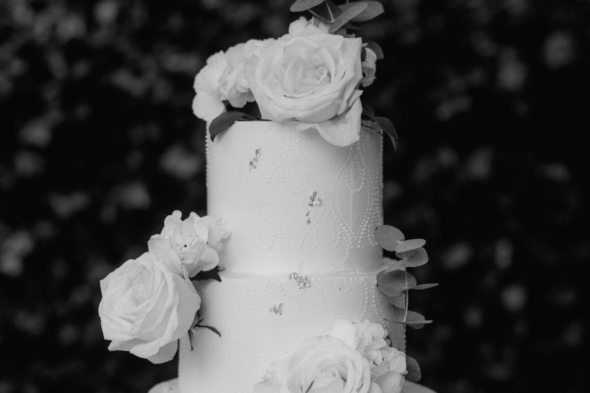 Black and white shot of the wedding cake with big roses on it.