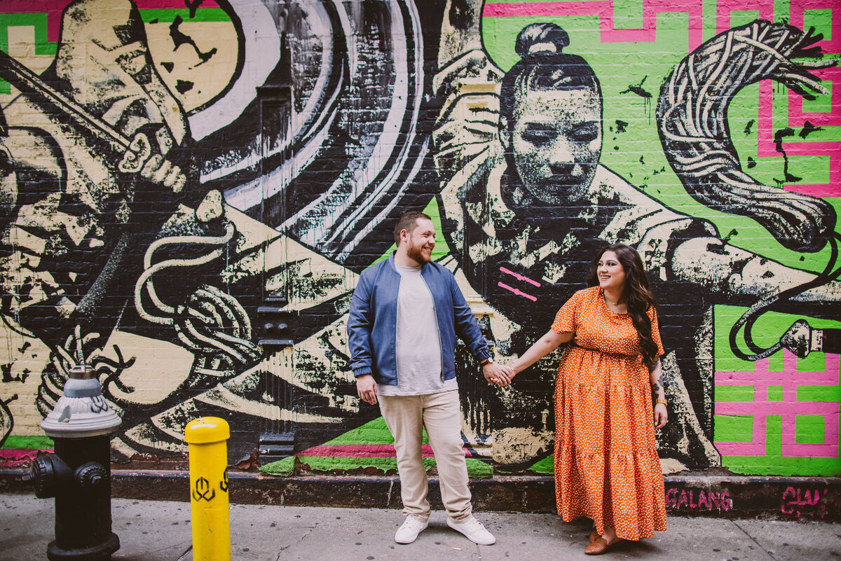 A couple laughing in front of a wall painting in chinatown nyc