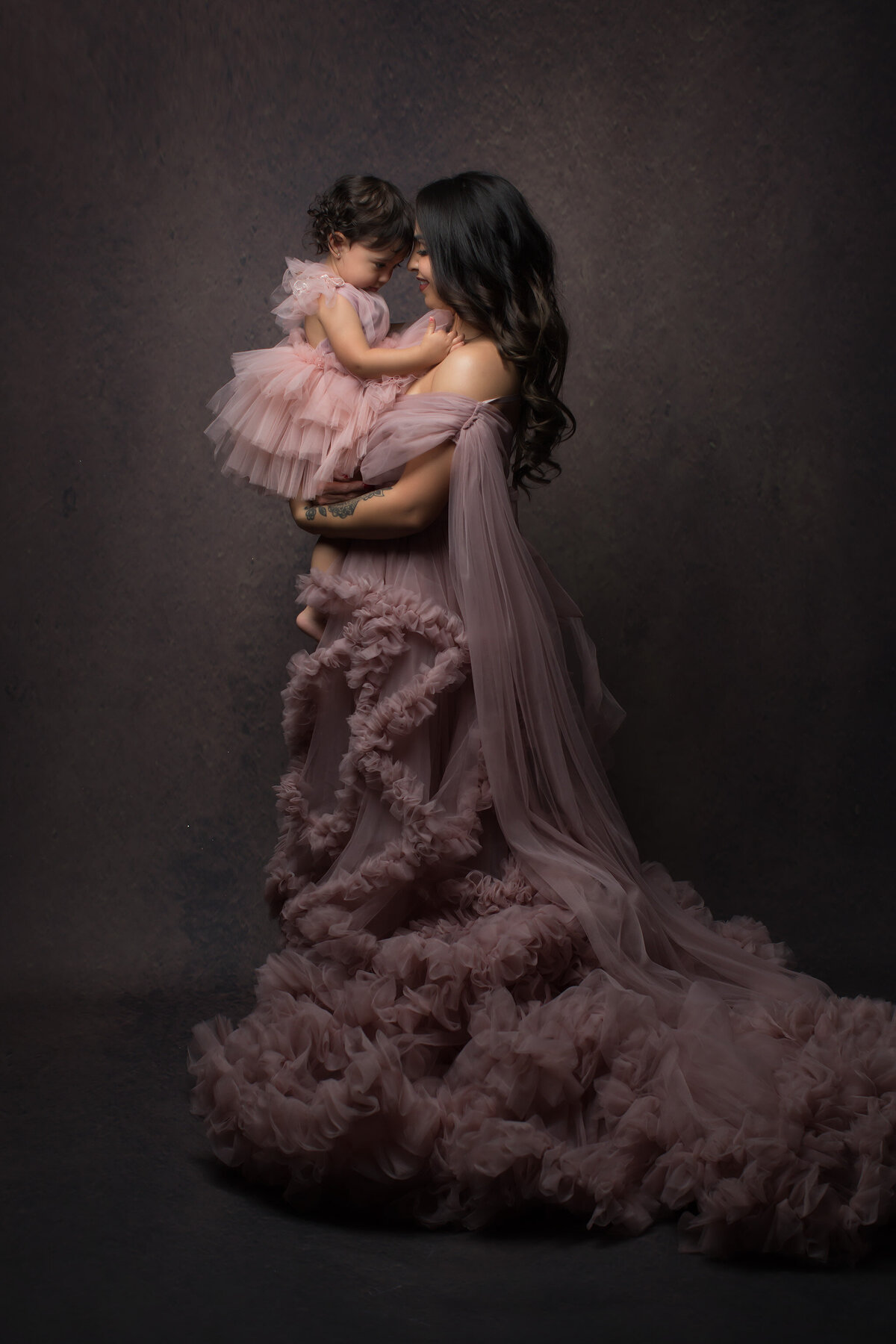 A mother and daughter share a joyful moment together, dressed in matching pink ruffled gowns, captured by a Dallas family photographer.