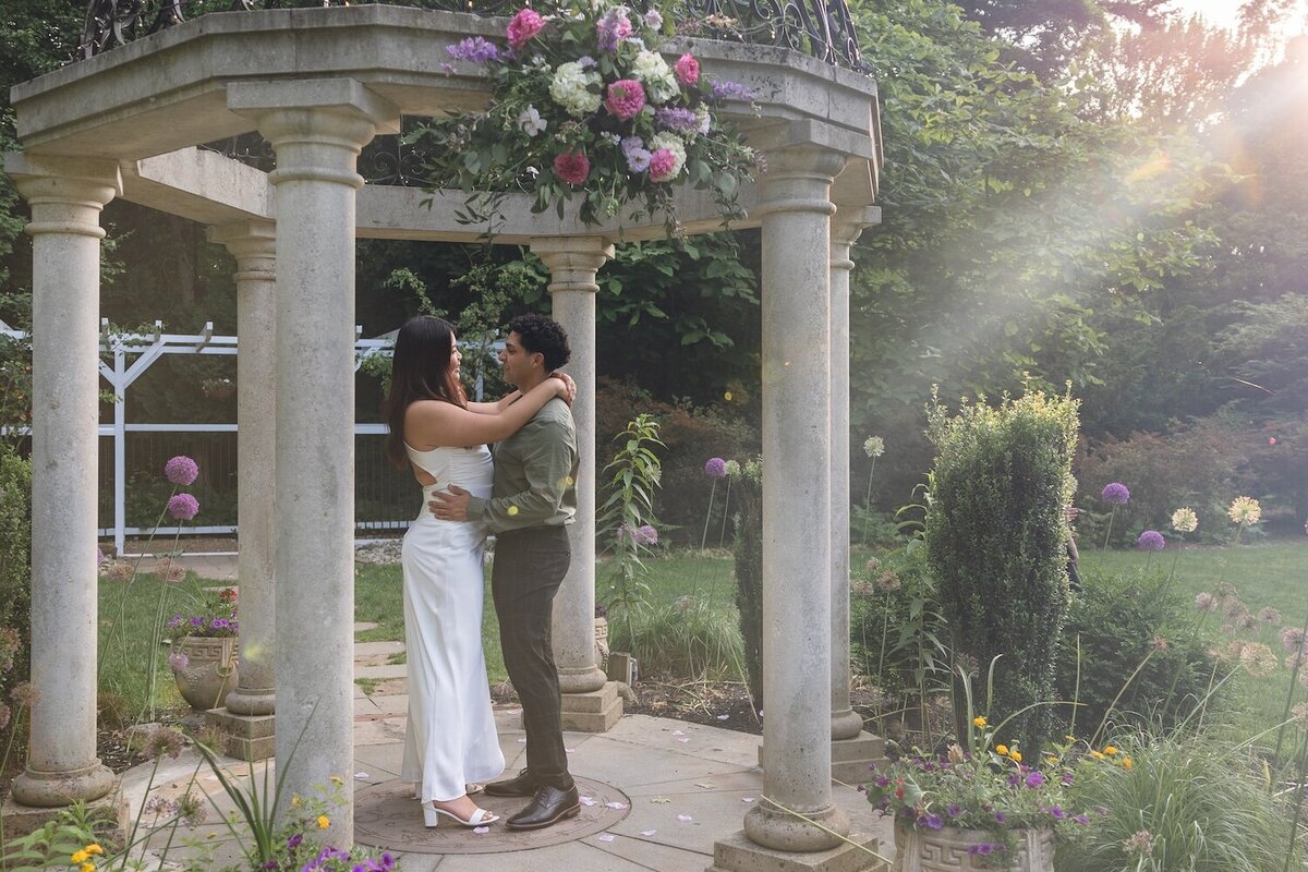 Romantic moment of couple standing under a sun-drenched pergola.