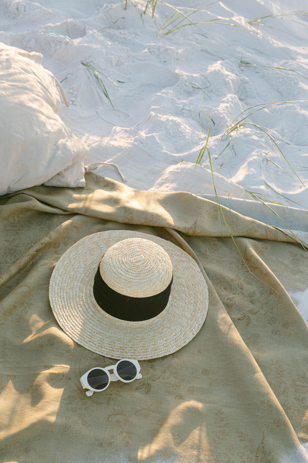 white Tol sunglasses and hat on a beige blanket.