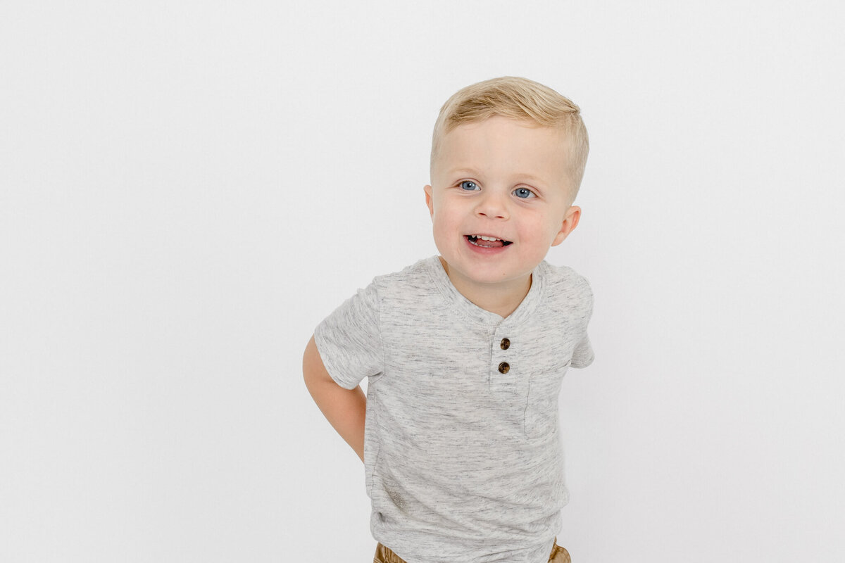 A little blonde boy wearing a gray buttoned shirt smiling while looking away from the camera at a studio in Tustin.