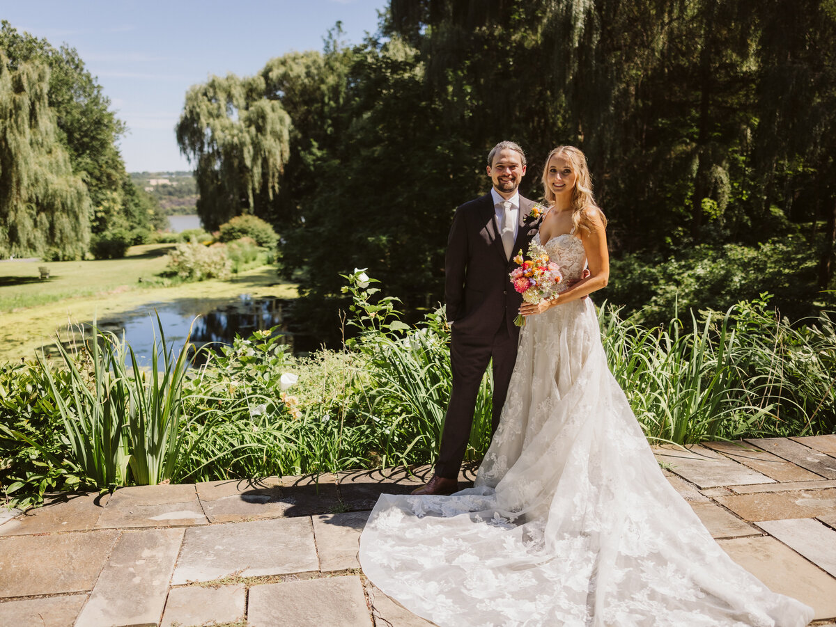 Bride and groom posing in front of pond at buttermilk falls inn, wedding planned by kr occasions 