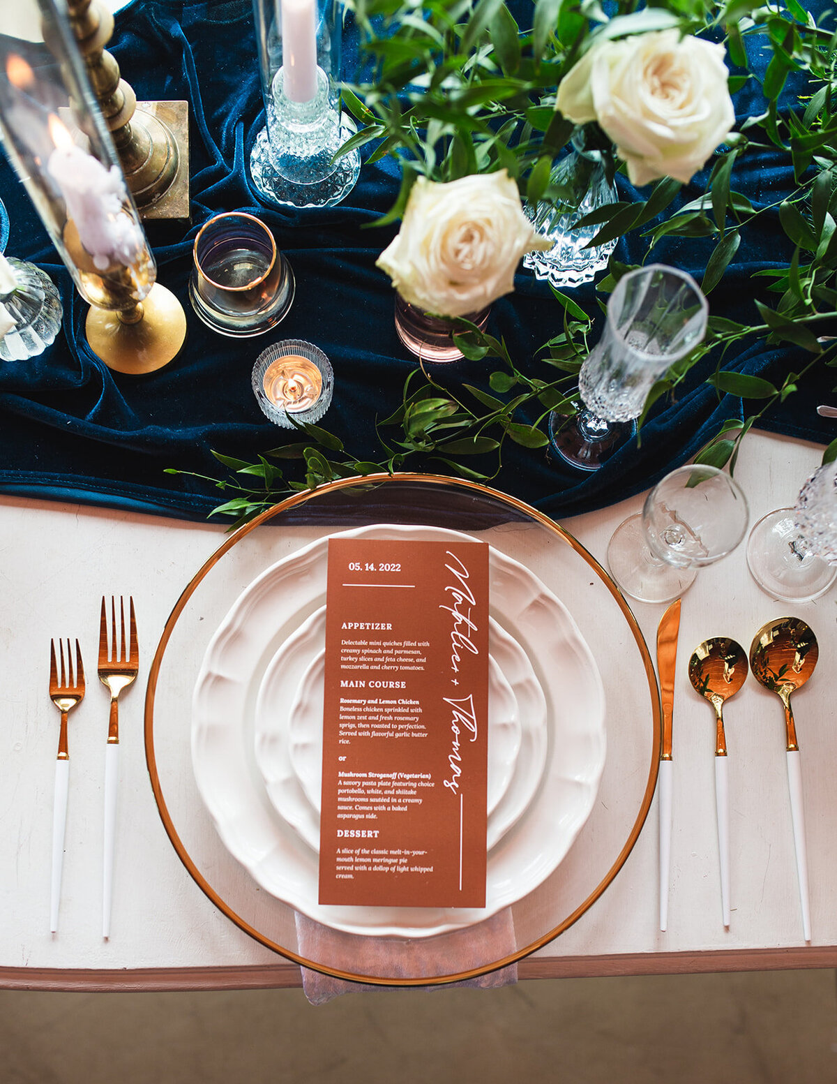 a plate, utensils, copper menu, and white roses sitting on a table