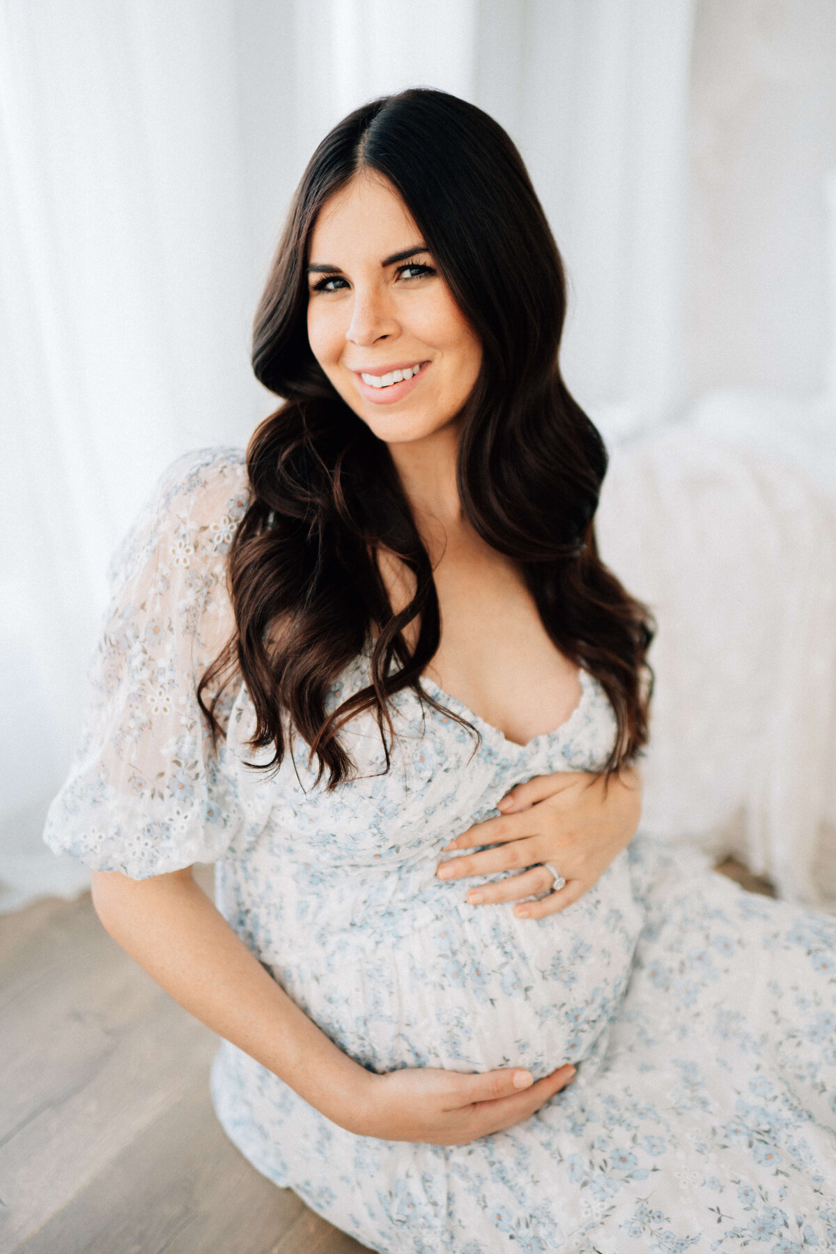 maternity mother sitting down and holding her belly while looking at Denver photographer