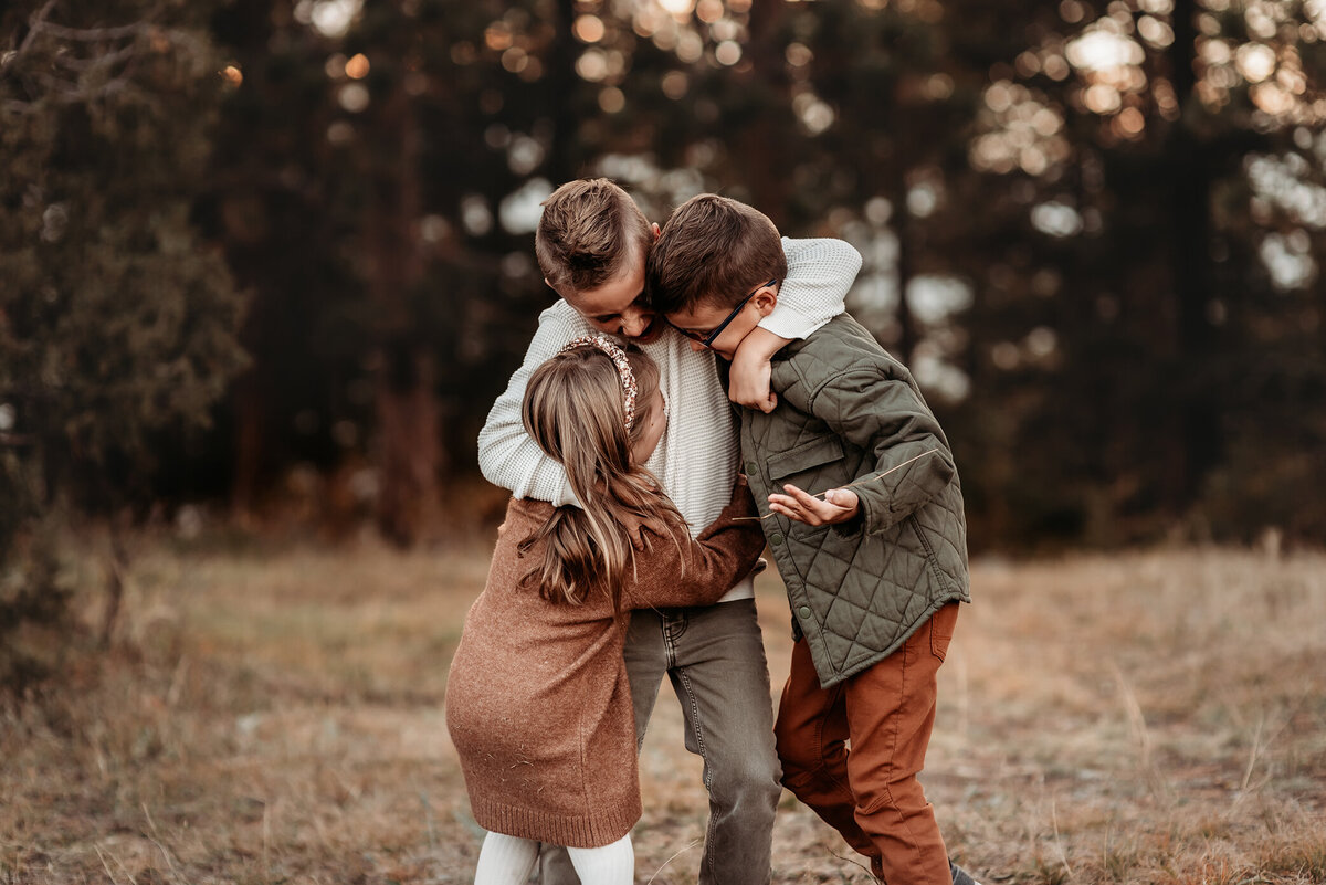 three siblings hugging each other tightly in the forest