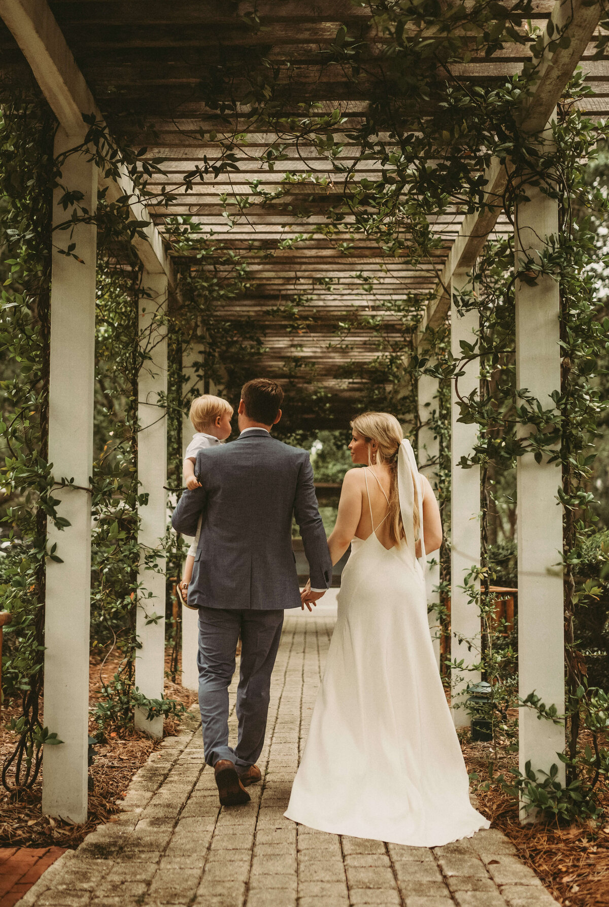 newlyweds & young son walk under garden arbor in rosemary beach florida