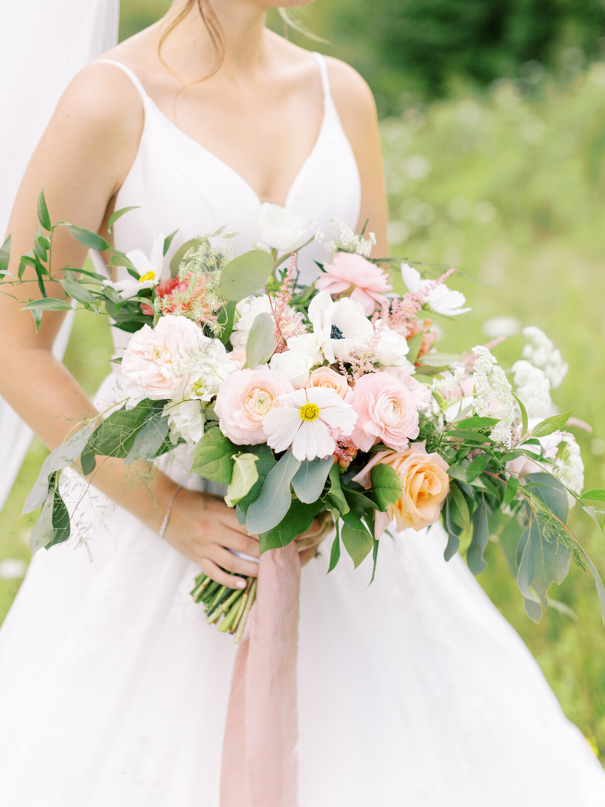 bride holding colorful whimsical bouquet with pink ribbon