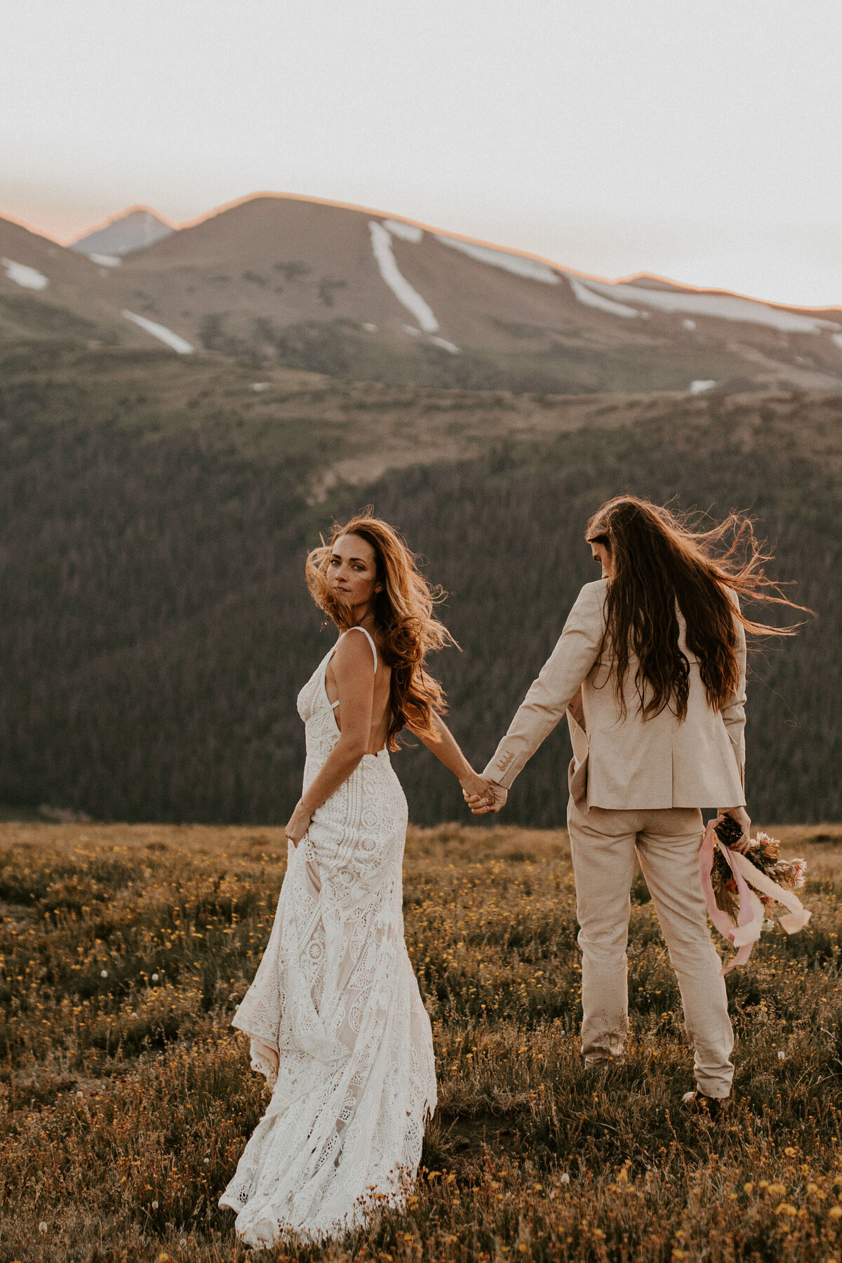 bride and groom wearing a white wedding gown and ivory tuxedo pose with a bouquet in the mountains