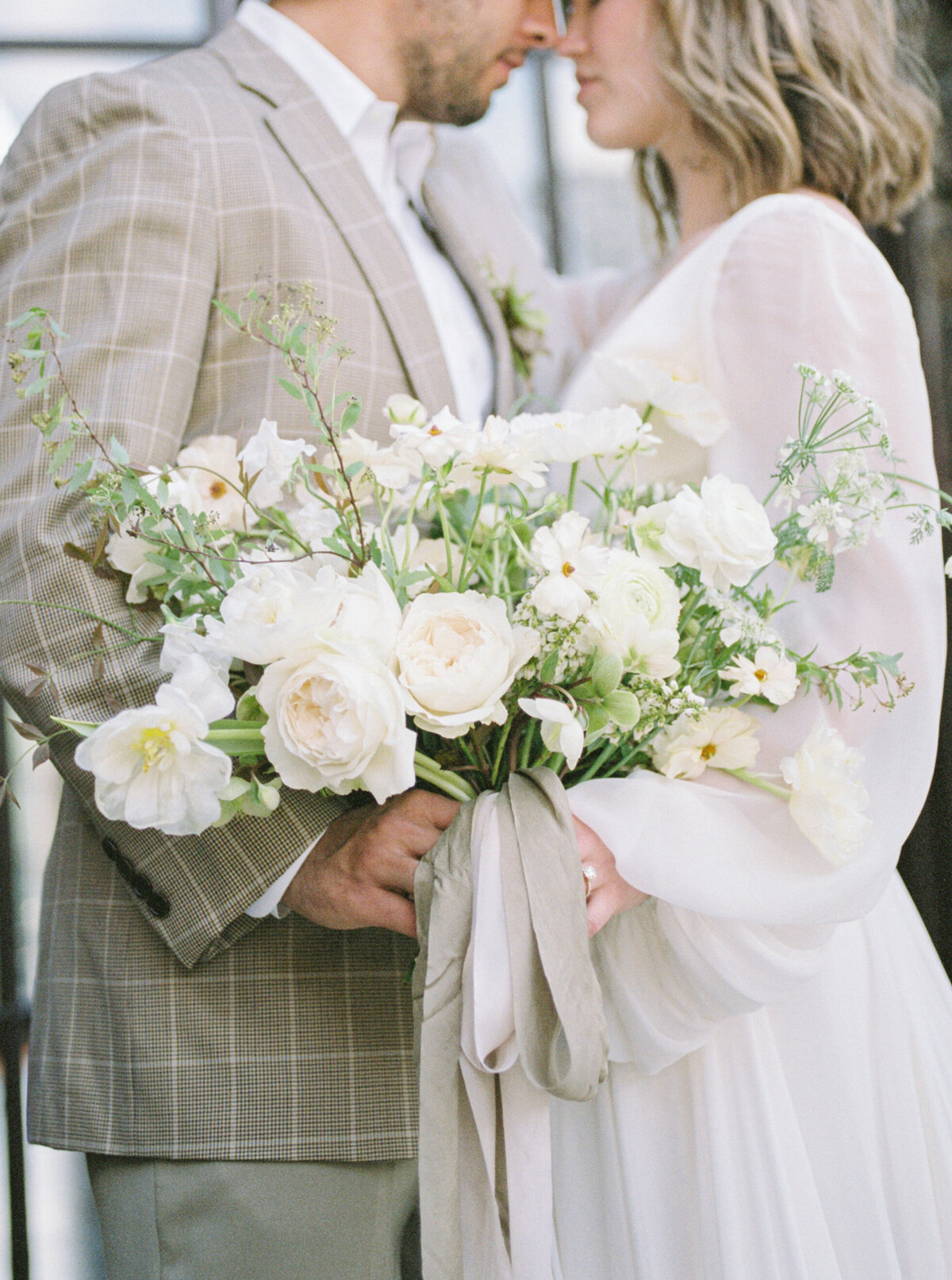 A bride and groom face to face as they hold the bouquet in the middle .