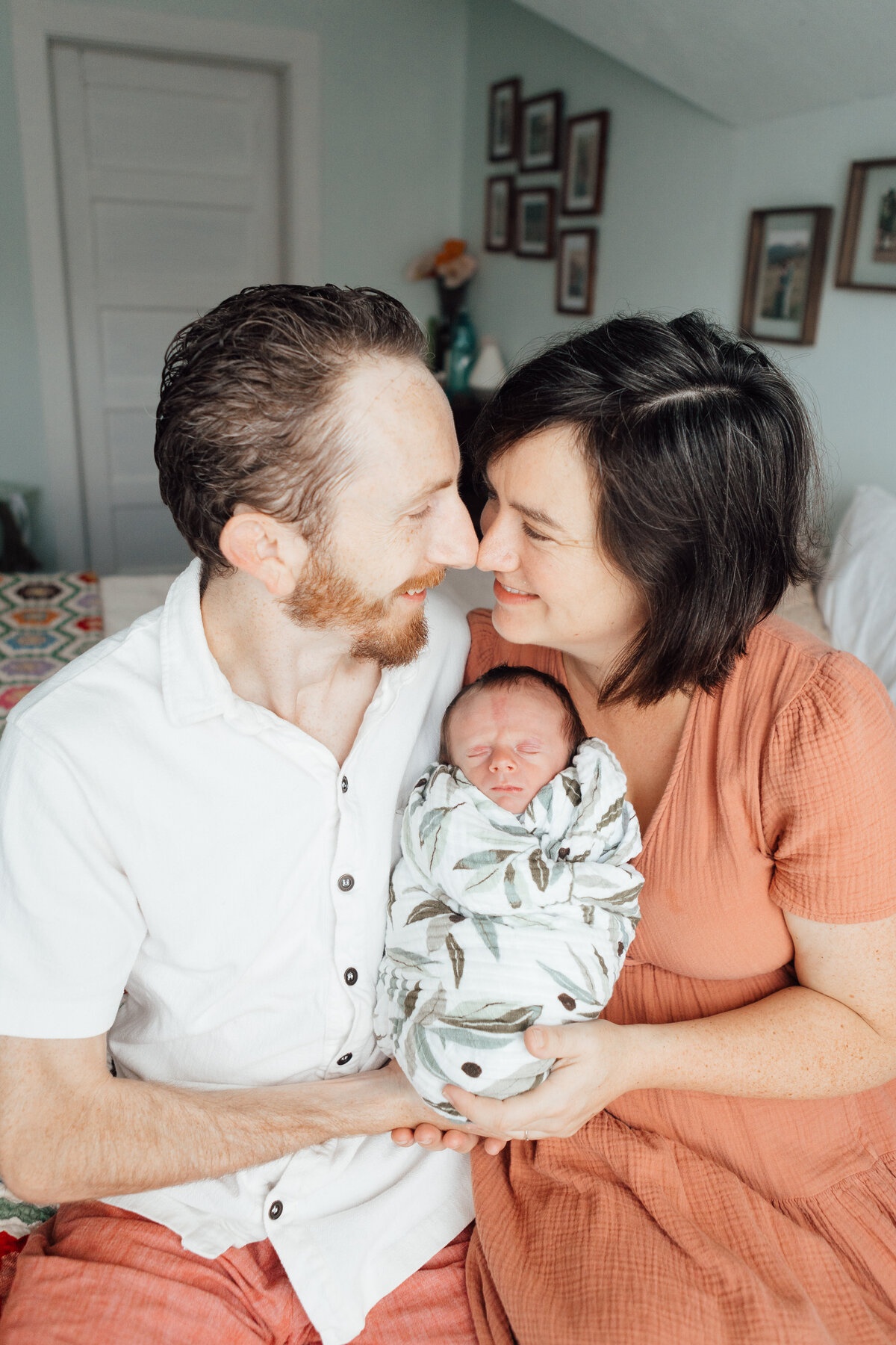 A man  and woman snuggle together holding their swaddled newborn son