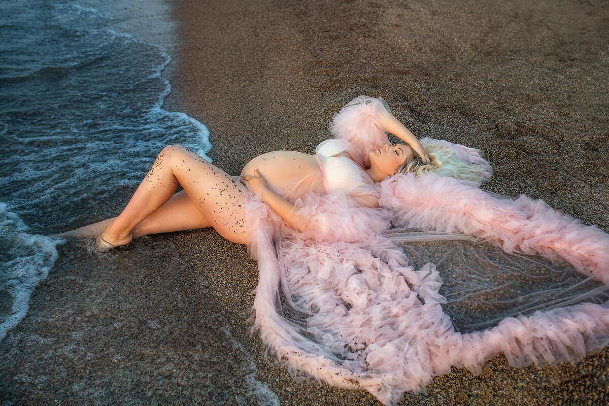 Washed to shore by beach waves pregnant  mommy in pink tulle maternity dress on the sand