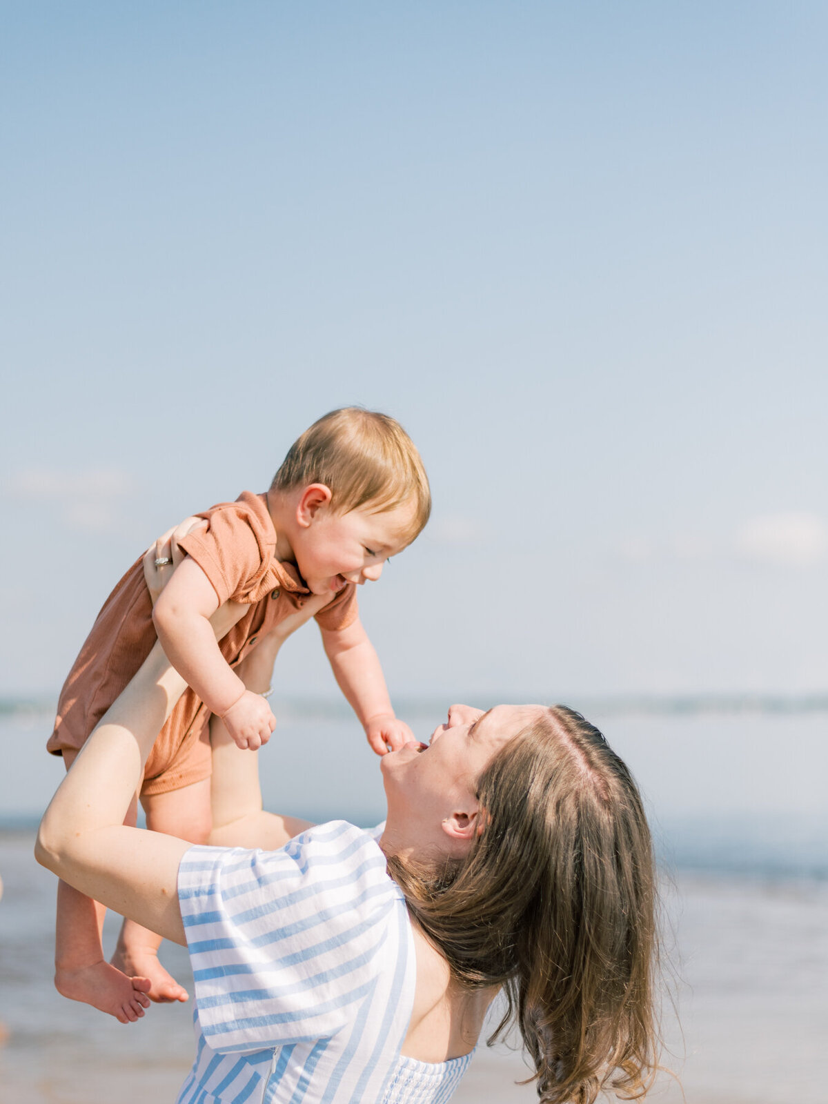 Mom holding her son up in the air while at beach.