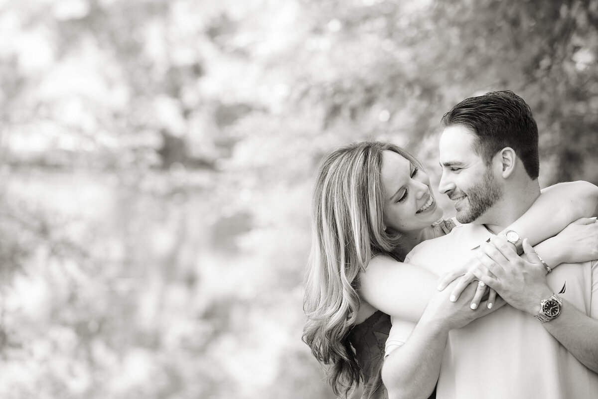 A person standing behind their partner as they hug them and smile 