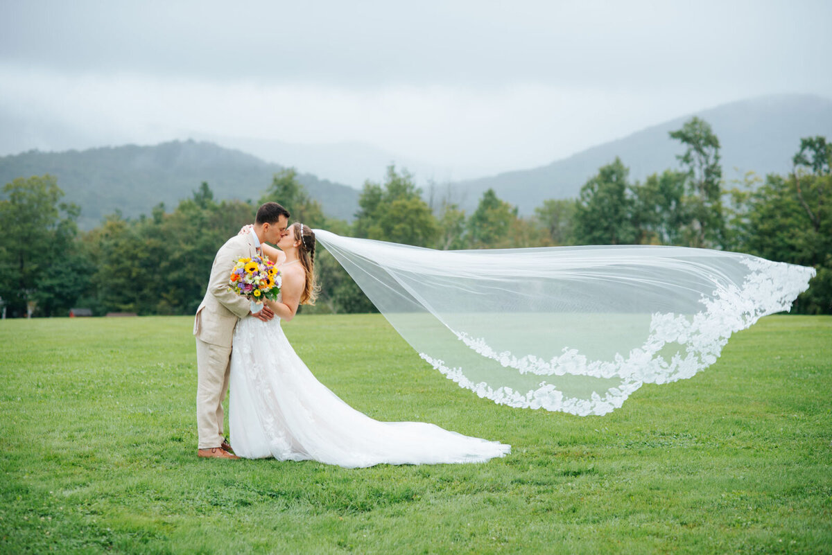 bride and groom kissing as veil blows in wind at rainy mountain top inn wedding chittenden vermont