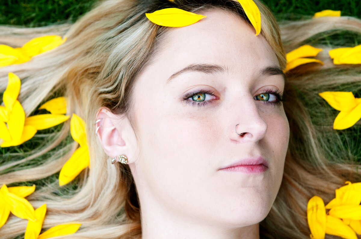 A close up of a person's face with yellow petals laying on her hair