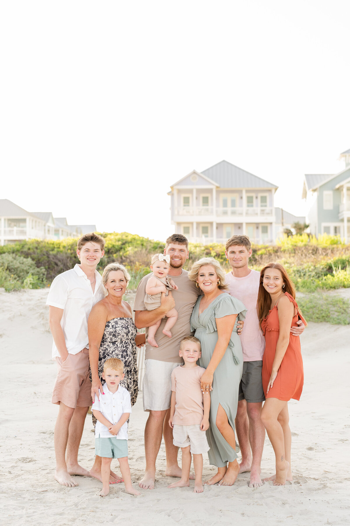 Large extended family smiling at camera  on beach in front of sand dunes with homes in the background