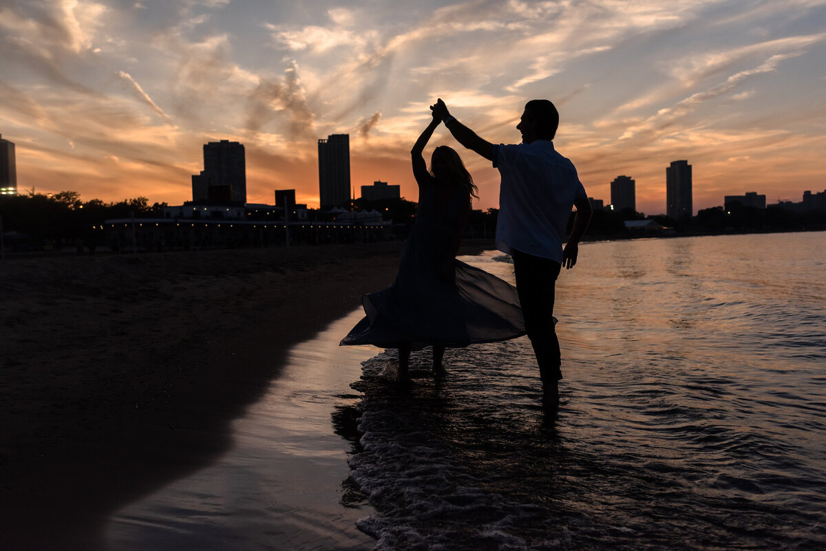 A man twirls a women in a dress while dancing in Lake Michigan at Sunset in Chicago