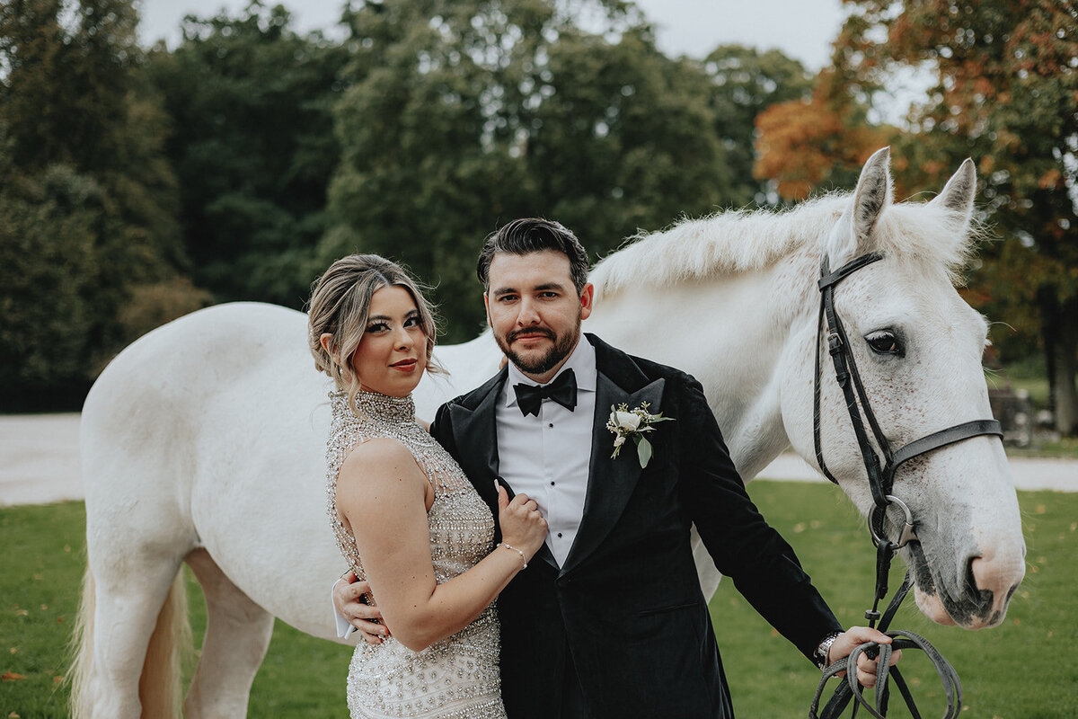 Bride and groom posing in front of white horse
