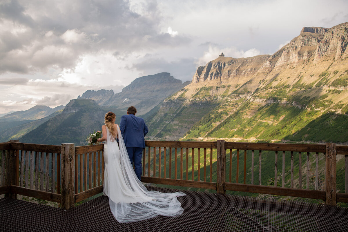 A bride and groom stand on a platform overlooking the mountains as their Montana elopement photographer takes their picture.