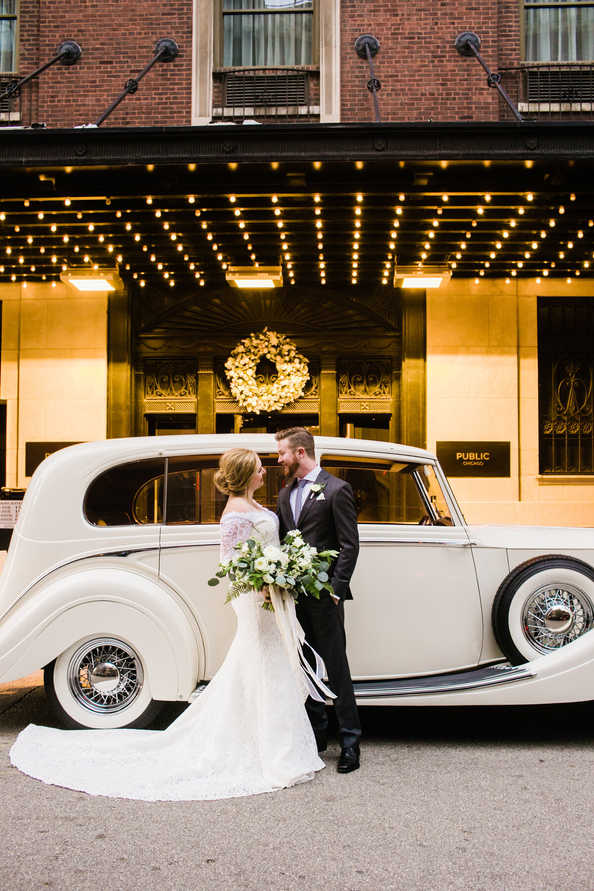 A stylish bride and groom posing in front of a vintage Rolls Royce, capturing timeless elegance and luxury on their wedding day.