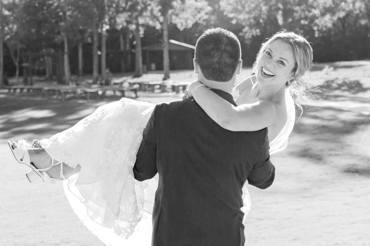 Groom carries bride while she laughs at the camera at charlotte wedding