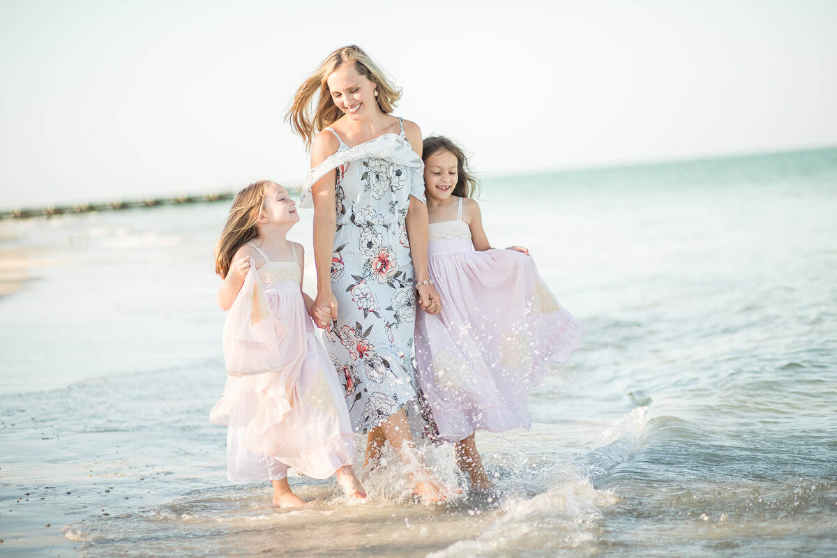 Blonde mother and two daughters walking and playing by waters edge at the beach in Siesta Key, FL 
