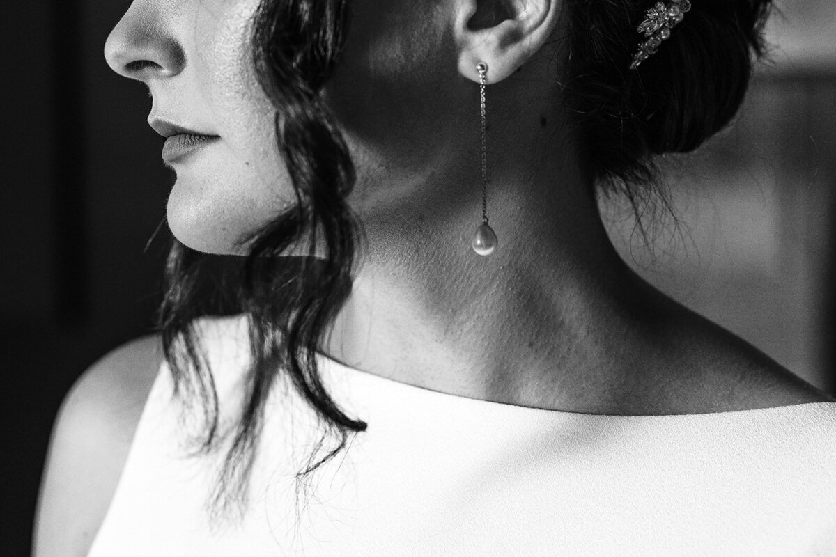A close up of a woman wearing a long earring with a pearl.