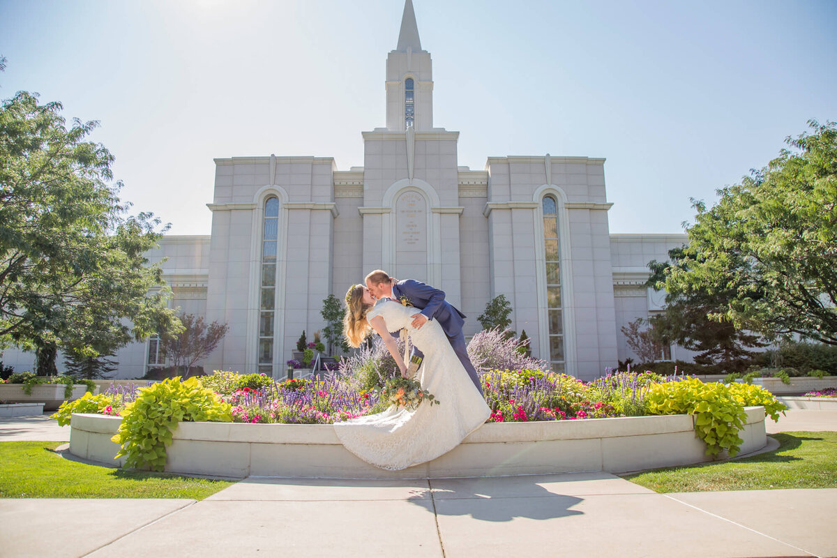 groom in blue suit dramatically dips bride in front of Draper Utah lds temple