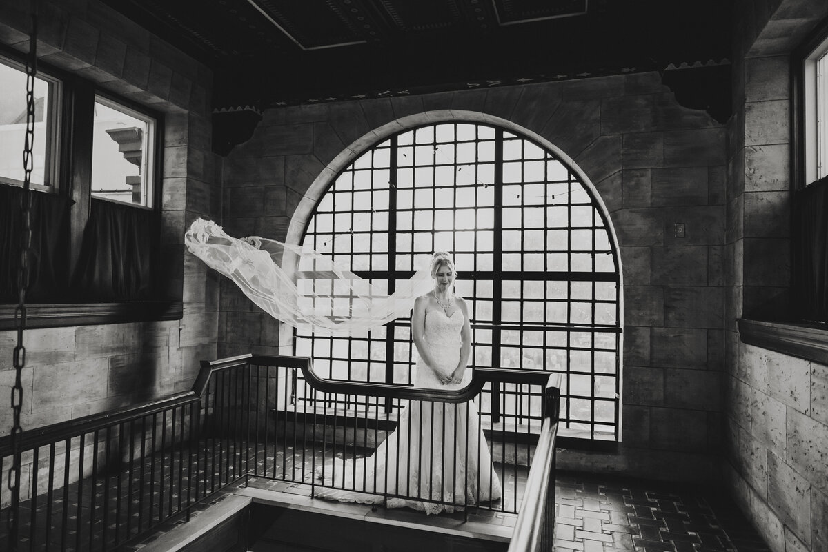Bride stands alone at Treasury on the Plaza with her veil floating dramatically in black and white under the arched window.
