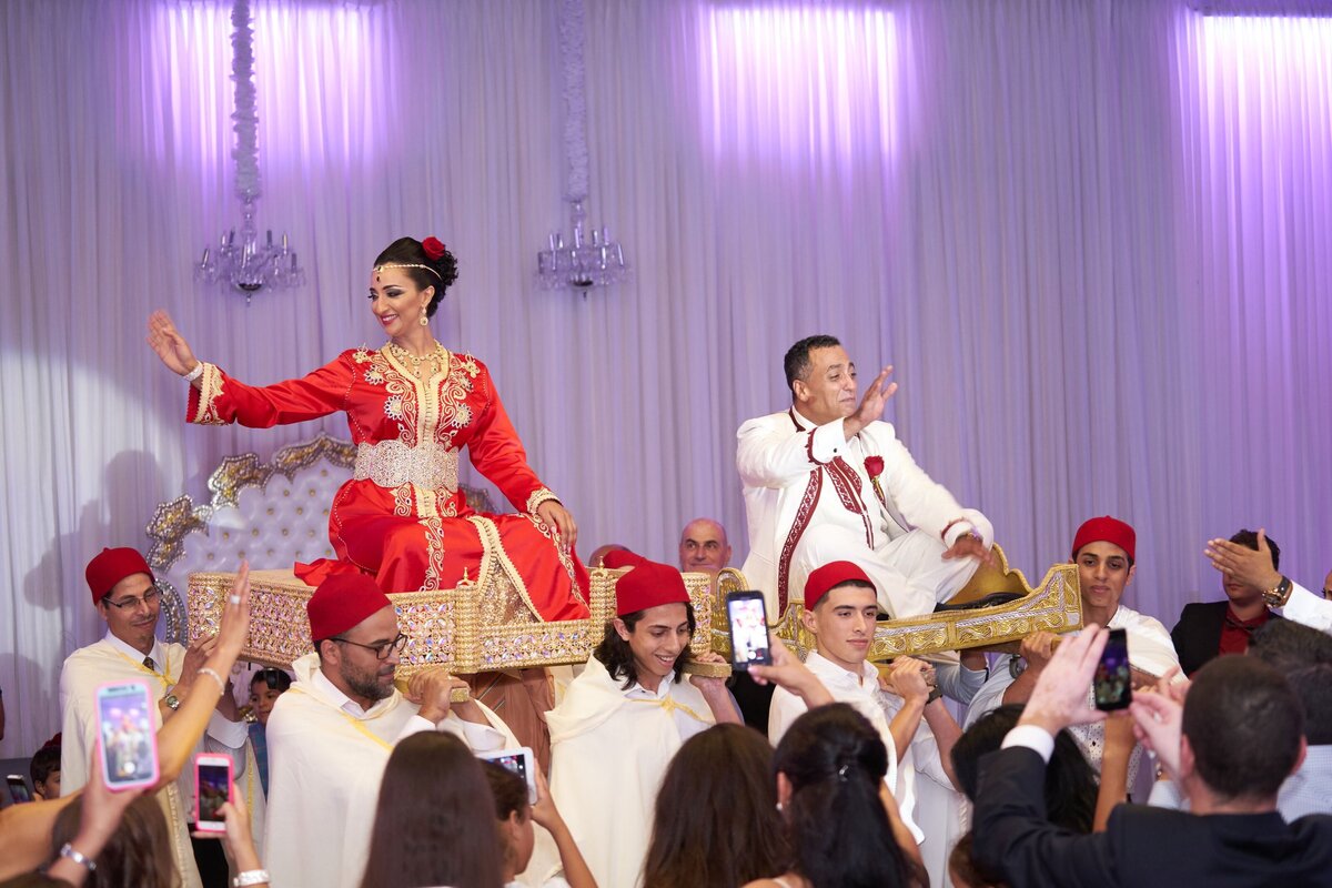 The bride and groom are joyfully lifted and carried by their wedding guests, celebrating their special day with playful and exuberant energy.