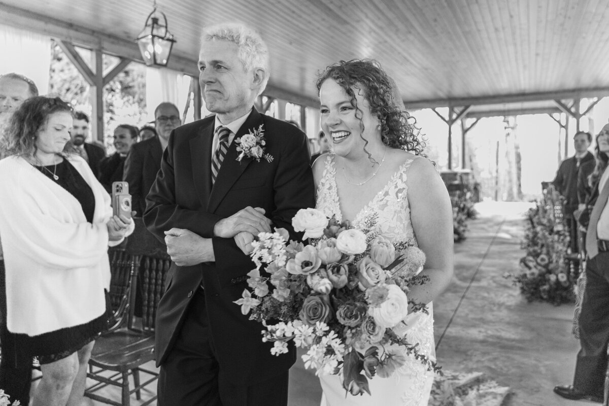 Black and white photo of a father walking his daughter down the aisle as she holds her bouquet
