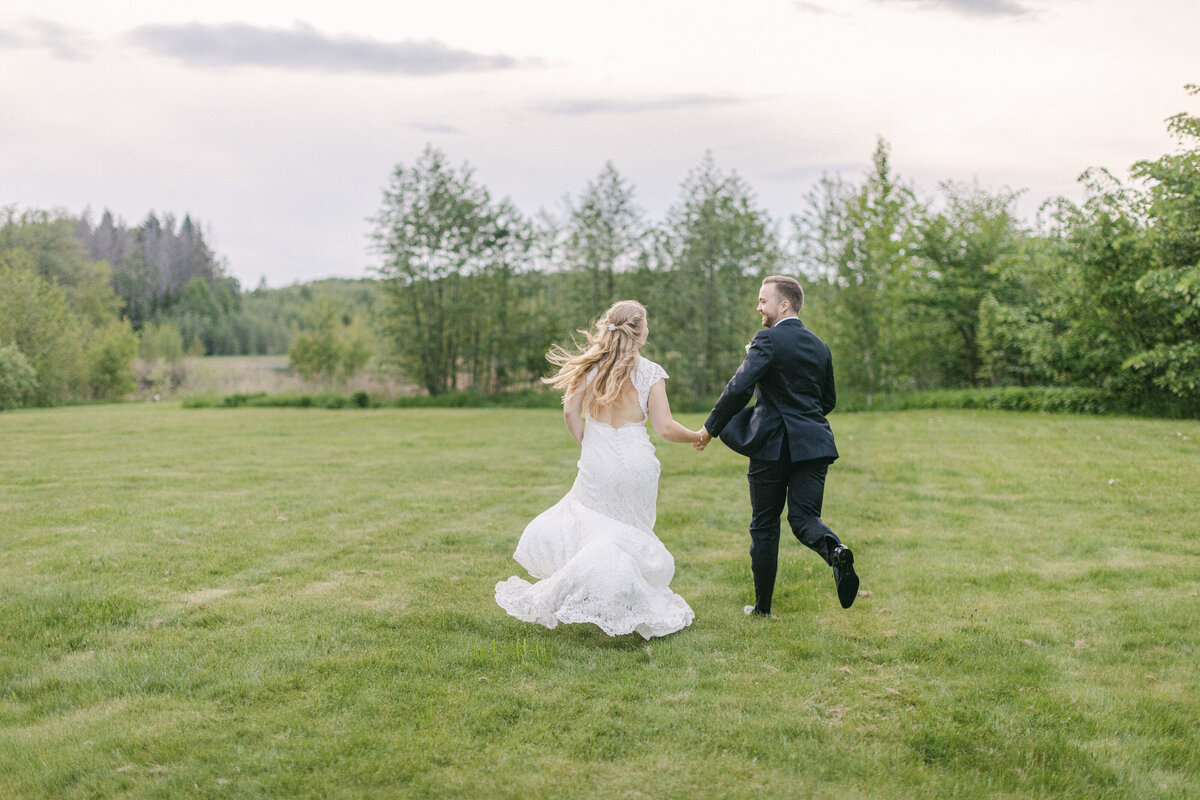 Bröllopspar håller varandra i händerna och springer på gräsmattan  vid Schenströmska