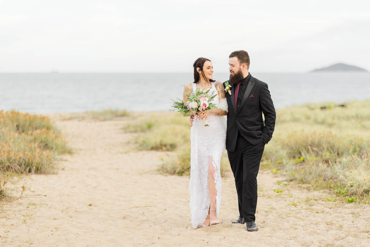 bride and groom walk along the beach dunes during golden hour portrait time.