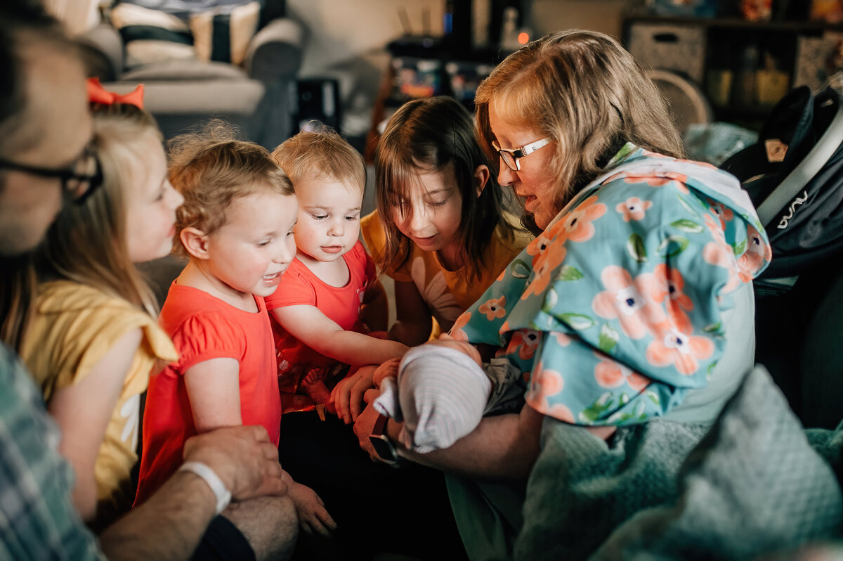 Mom holding newborn baby around for young children.