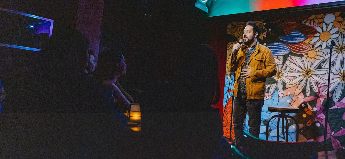 Ahmed Bharoocha on stage, holding a microphone, in front of a flower background