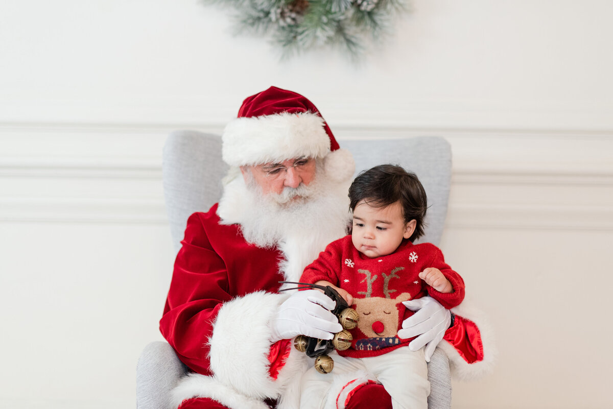 santa with toddler boy ringing sleigh bells toddler siblings brother and sister jumping on the bed with snow and pajamas by miami christmas mini session photographer msp