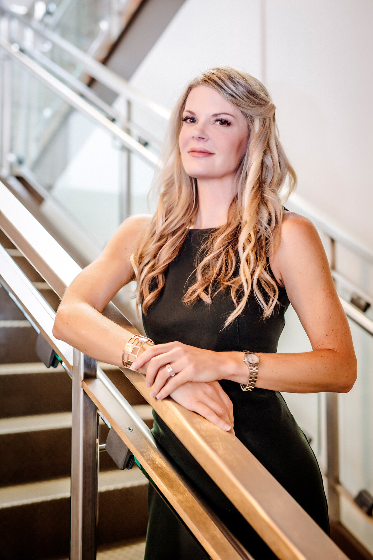 A Female Nurse Practitioner wearing a black dress, standing on a modern stairwell, posing for a South Shore MA branding photographer