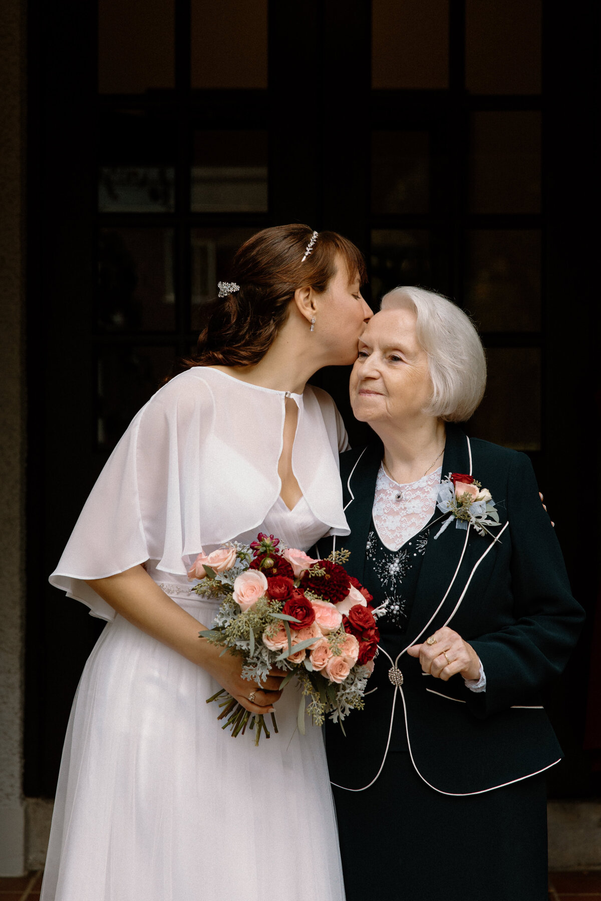 The bride kissing her grandma's forehead while her grandma smiles