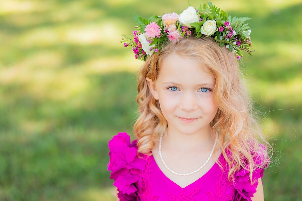 Flower girl wearing a hot pink dress with puffed sleeves and a vneckline is wearing a flower crown with light pink tea roses, red berries and white tea roses accented with fern and greenery at Sugarfoot.