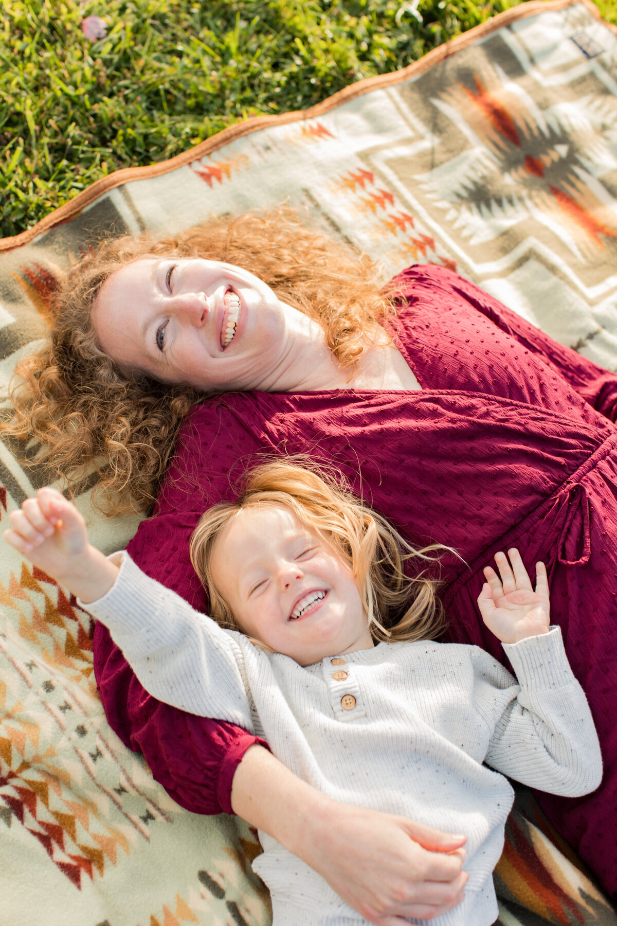 Family photo in Banner Elk, NC of a mom lying on a blanket with her toddler son and laughing at the camera during a family photo session.