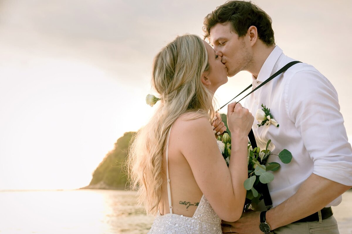 Couple kissing in the elopement  photoshoot  and the sunset behind them on Phuket beach