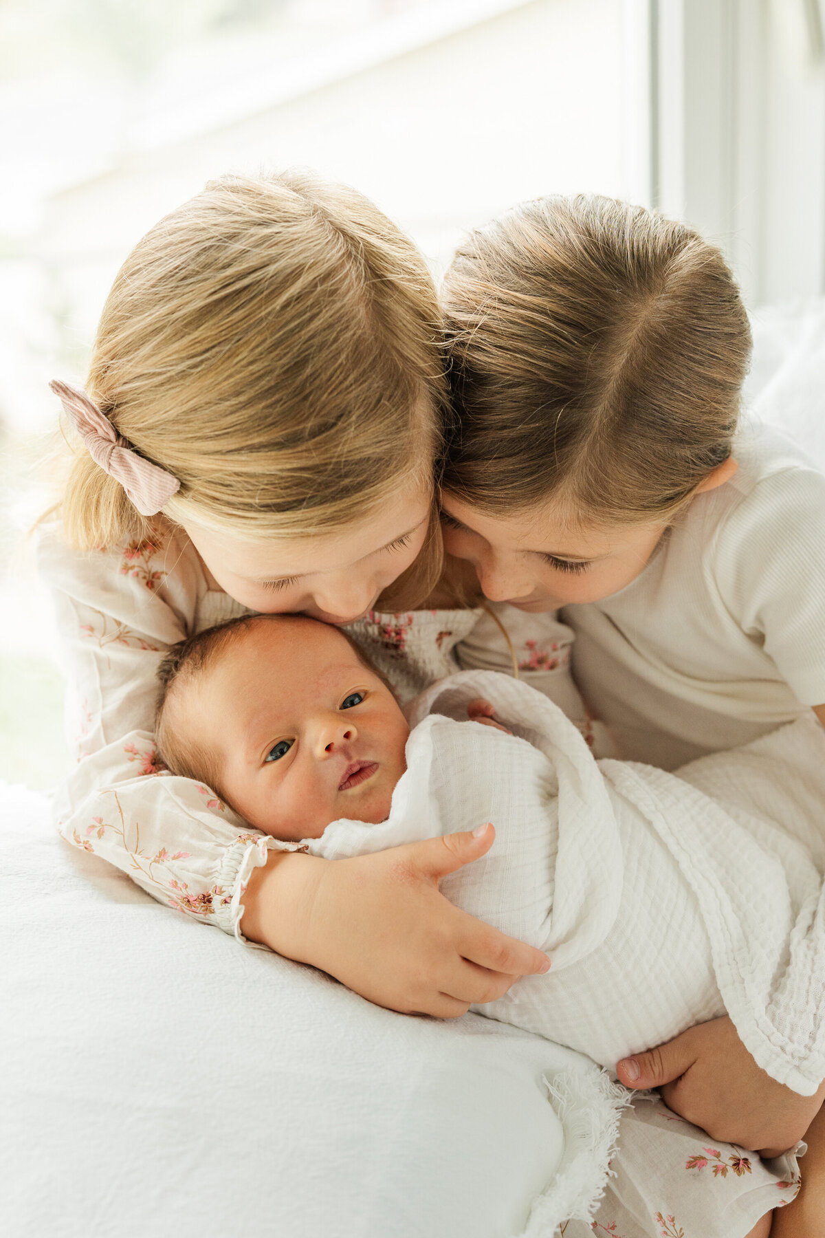 Two siblings gently cuddling their newborn baby brother, sharing a loving and protective moment together