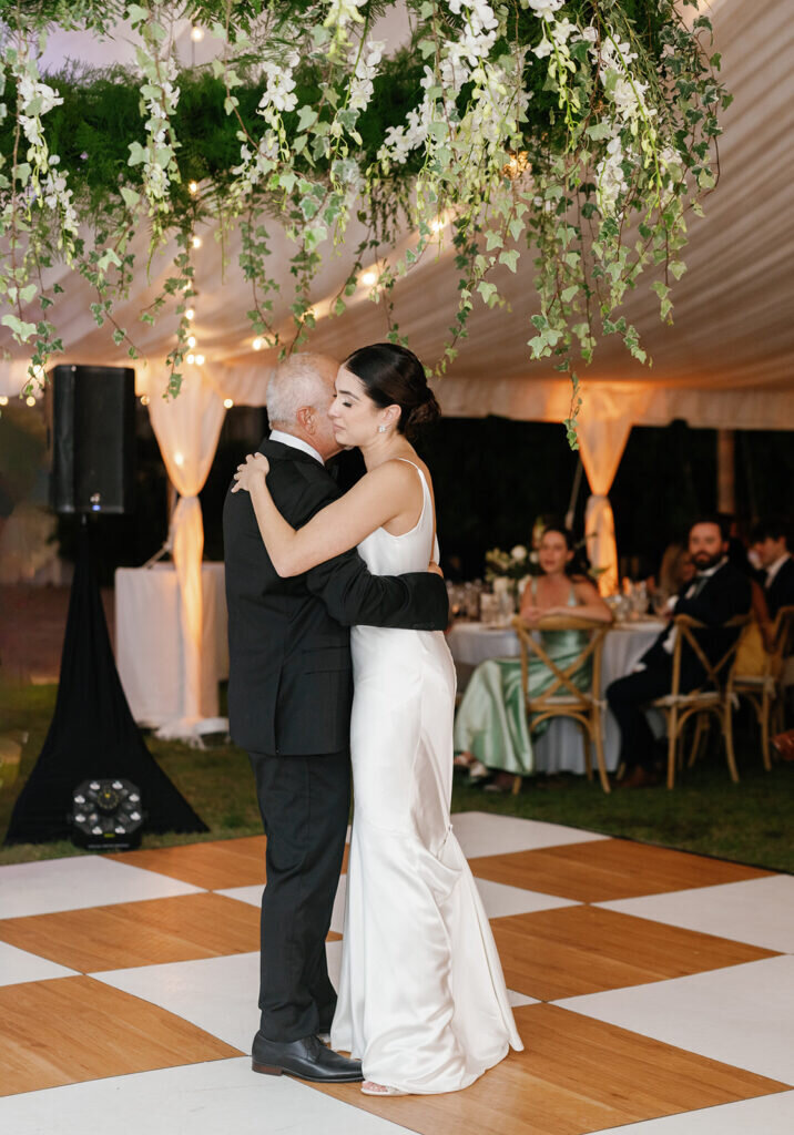 A heartfelt moment as the bride shares a special dance with her father on the checkered dance floor, surrounded by wedding guests under a beautifully decorated tent. Captured by Claudia Amalia Photography, a Florida Keys wedding photographer.